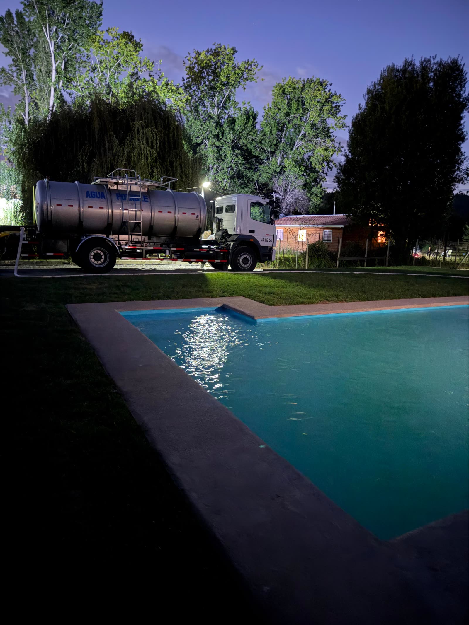 Camión aljibe llenando una piscina al atardecer